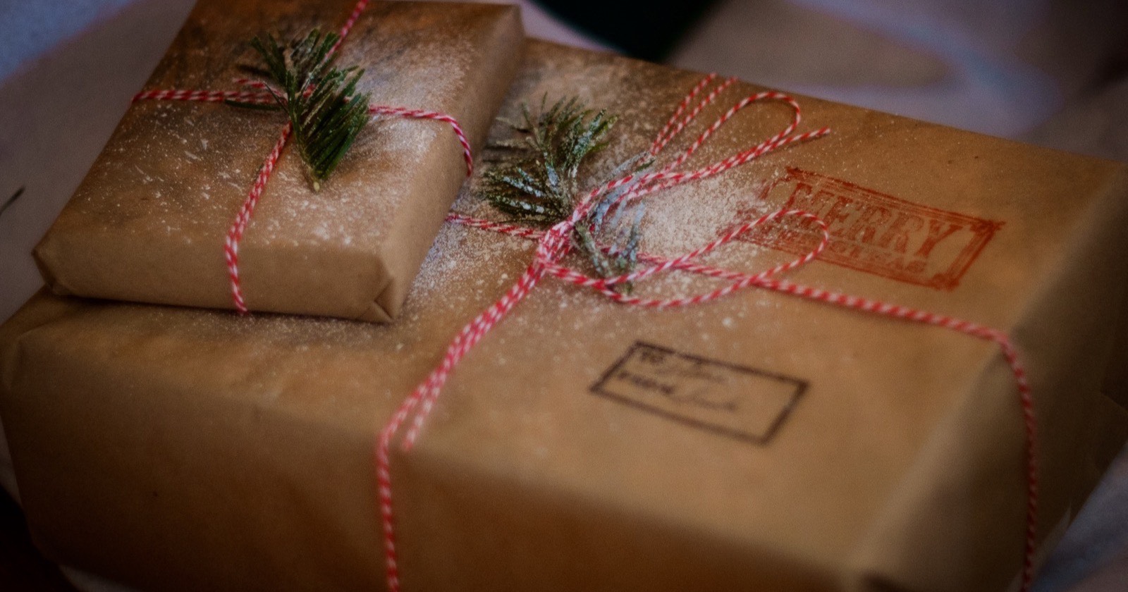 Zwei in braunes Packpapier eingeschlagene Päckchen mit rot-weißer Kordel, Tannenzweigen und rotem Weihnachtsstempel