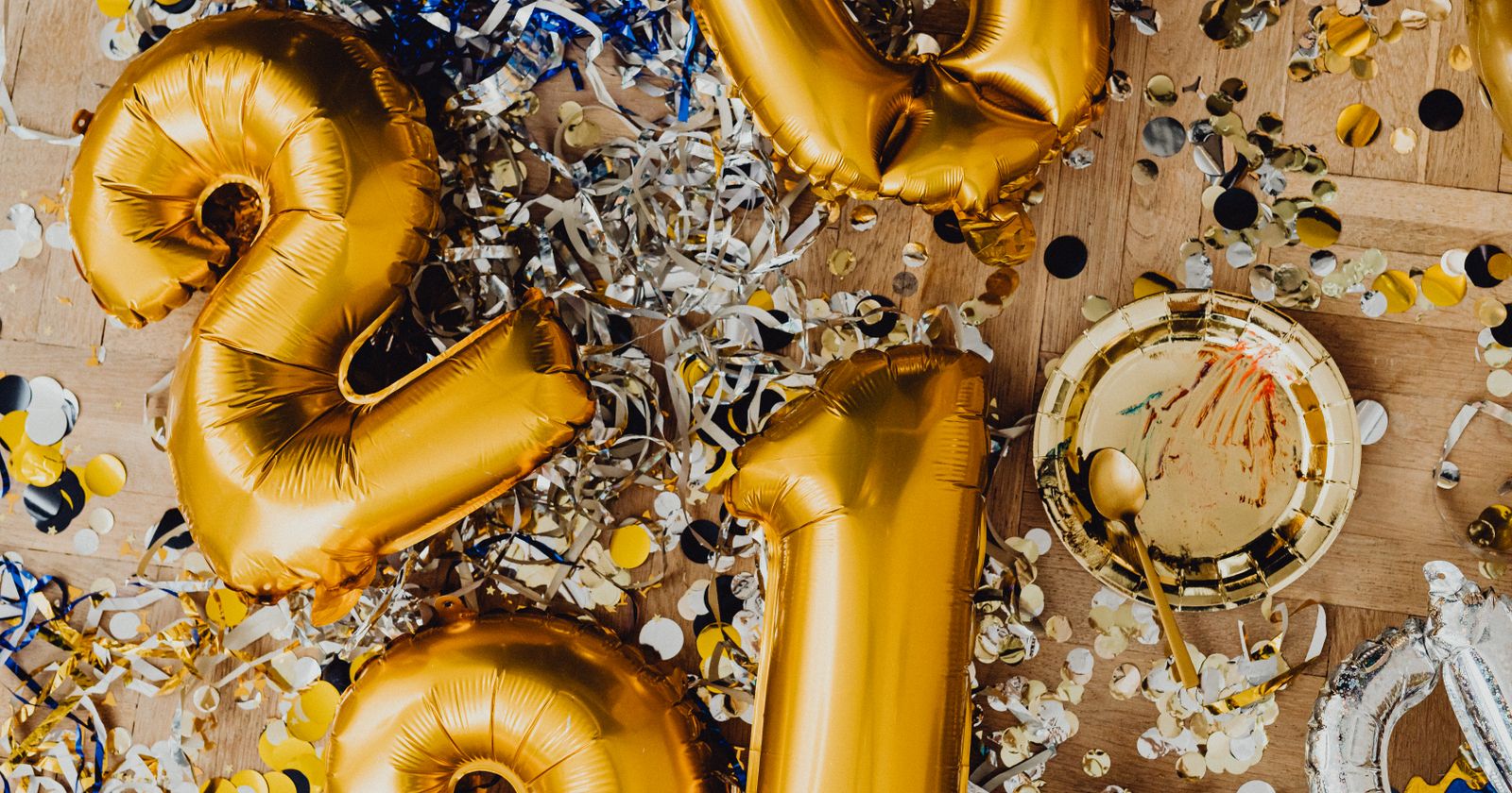 Goldene Zahlenballons zwischen Konfetti und Luftschlangen auf einem Holzboden nach einer Feier